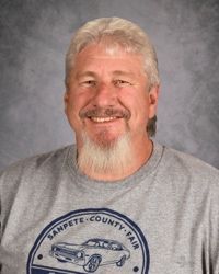 Smiling man in gray T-shirt with a classic car graphic against a gray studio backdrop