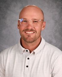 Portrait of a smiling bald man in glasses and a white polo shirt against a gray background