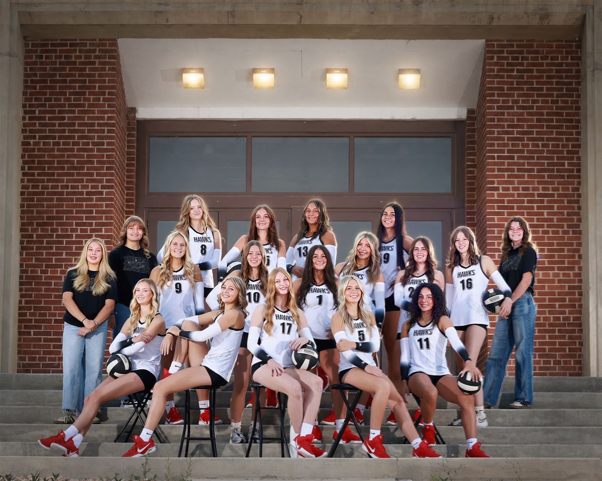 Group of volleyball players posing on steps outside a brick building, wearing white and black uniforms.