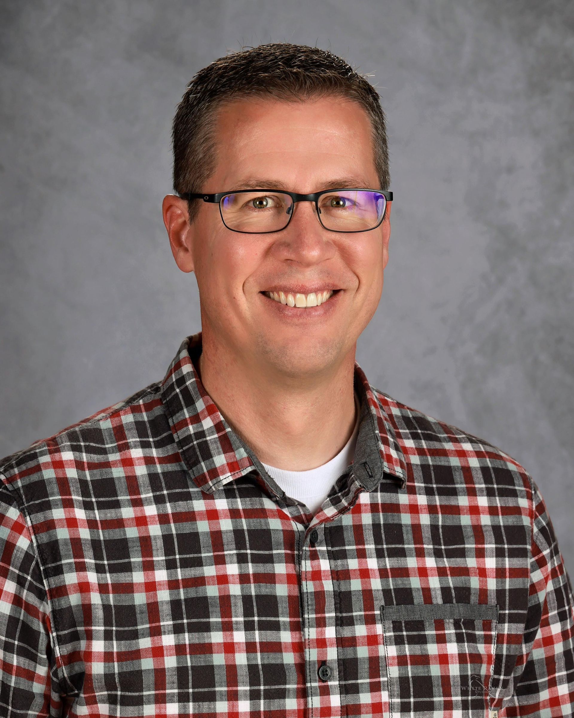 Man wearing glasses and plaid shirt smiles at camera.