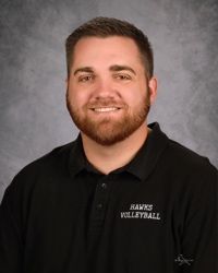 Portrait of a smiling man in a black “Hawks Volleyball” polo against a gray studio backdrop