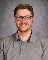 Portrait of a smiling person wearing glasses and a gray polo shirt against a gray studio backdrop