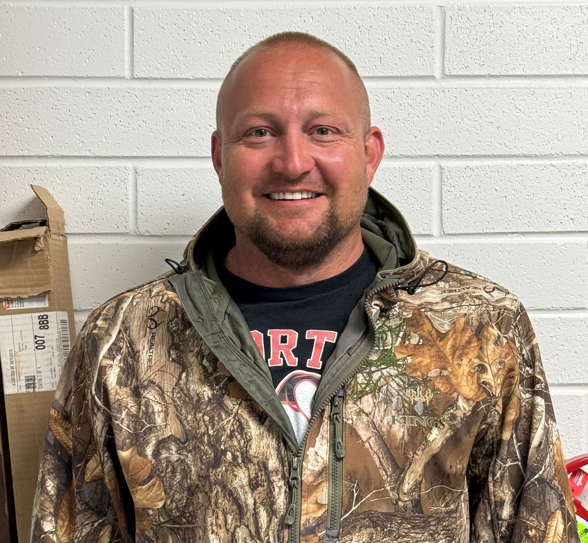 A man wearing a camo jacket and a shirt that says rt