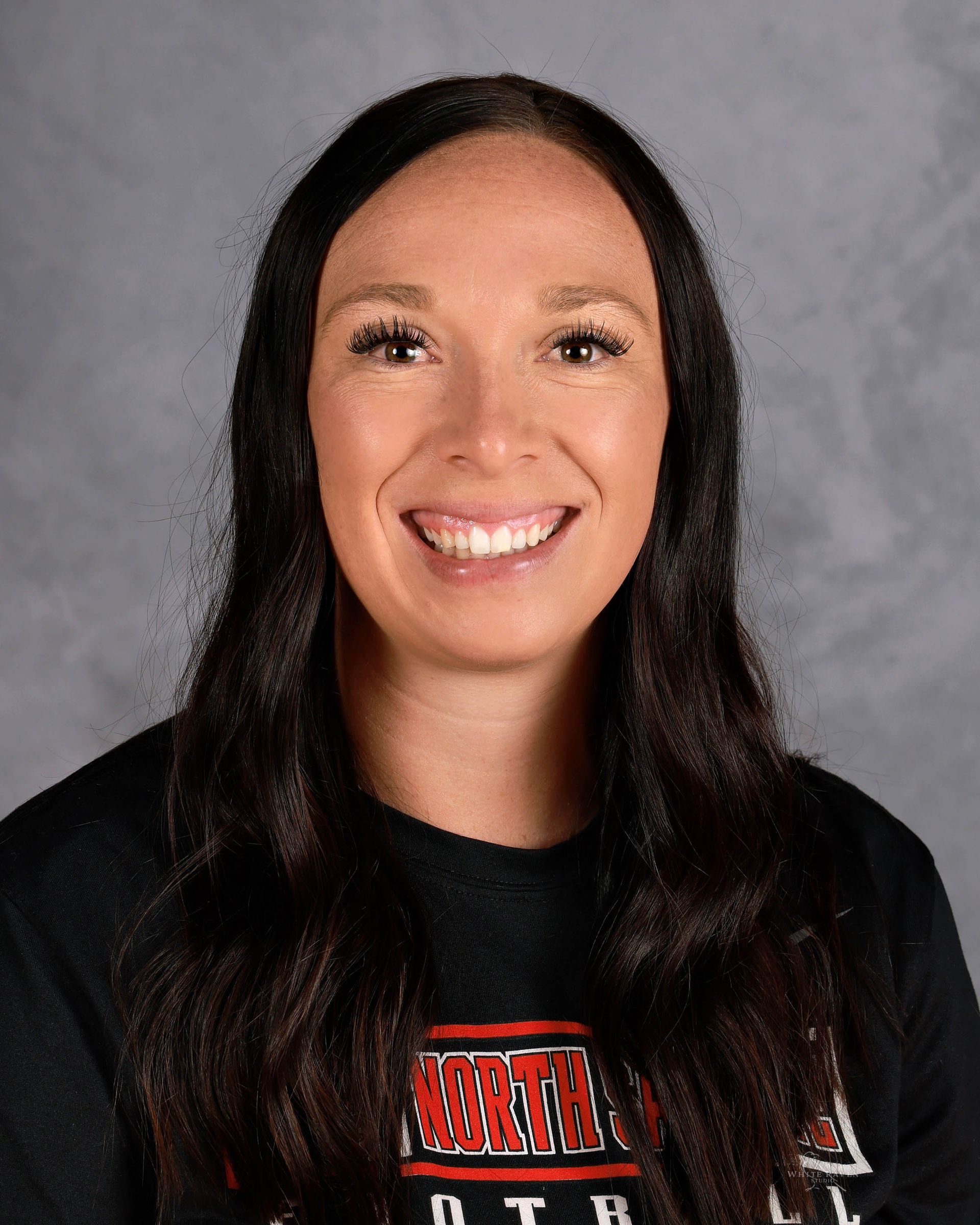Woman with long dark hair smiles, wearing a black shirt with 
