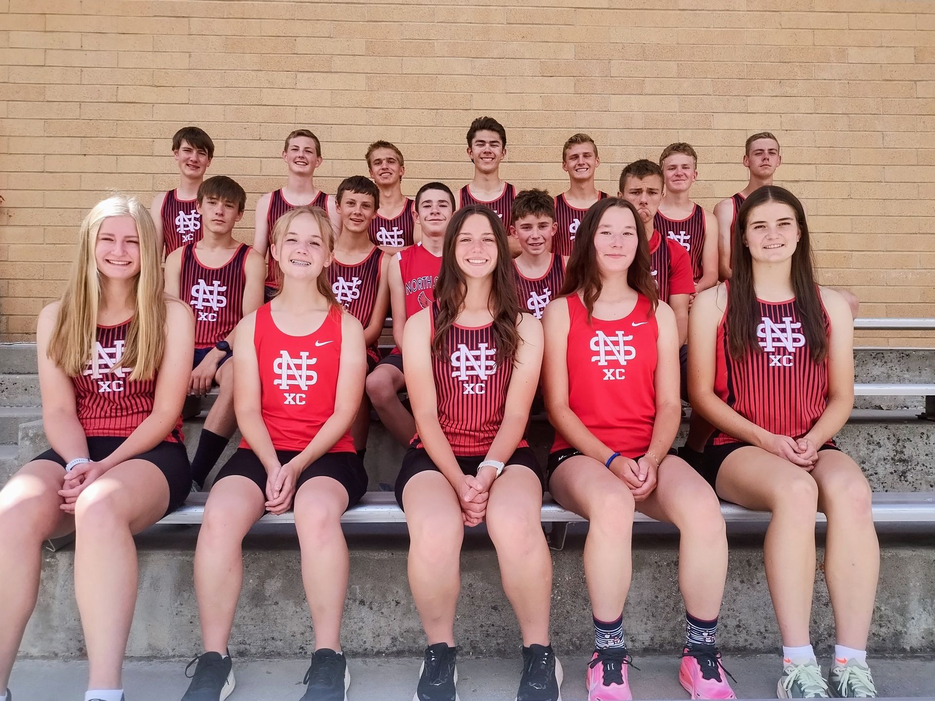 Group of athletes in red uniforms posing on bleachers against a brick wall
