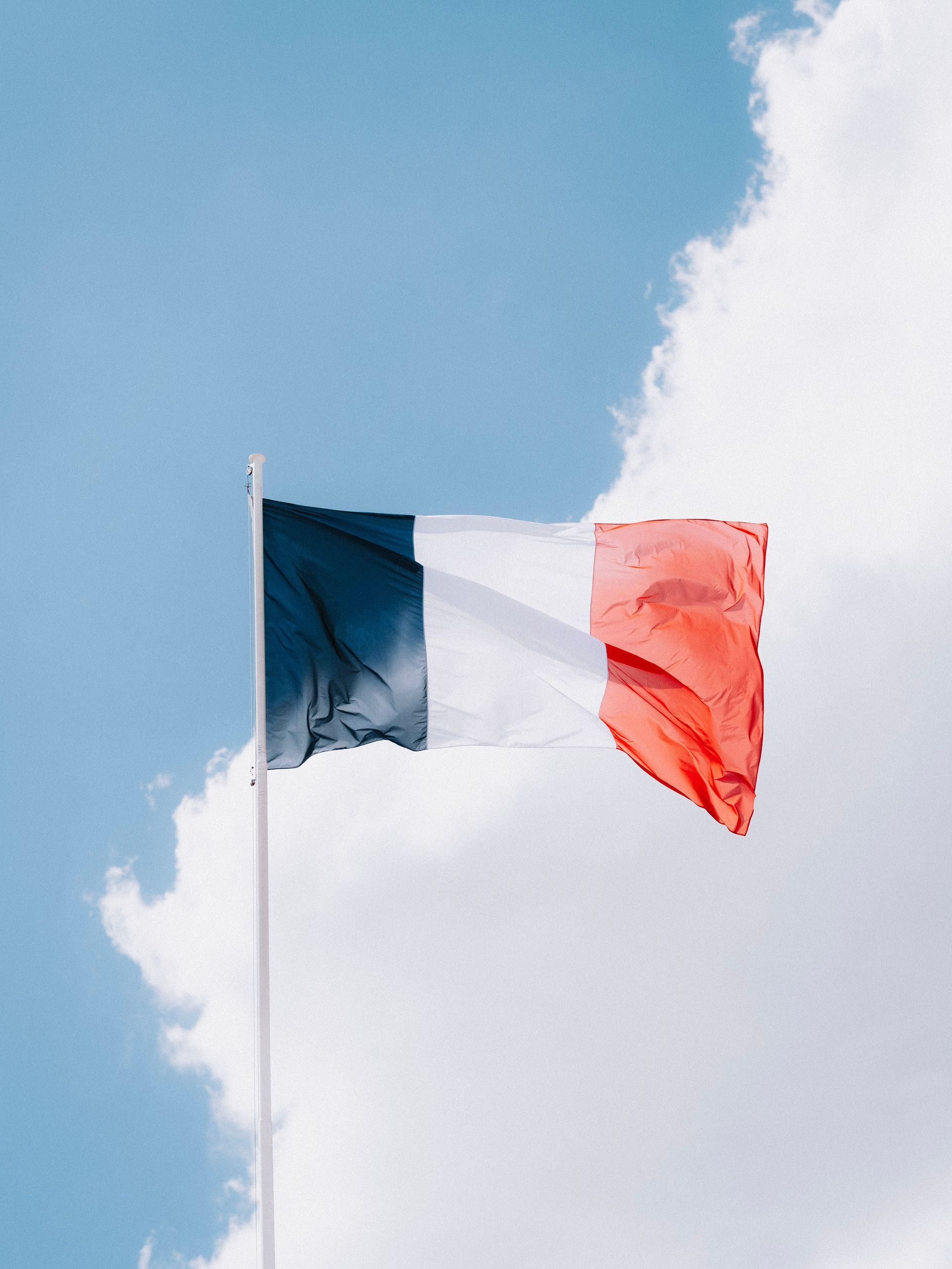 French flag waving against a blue sky with clouds