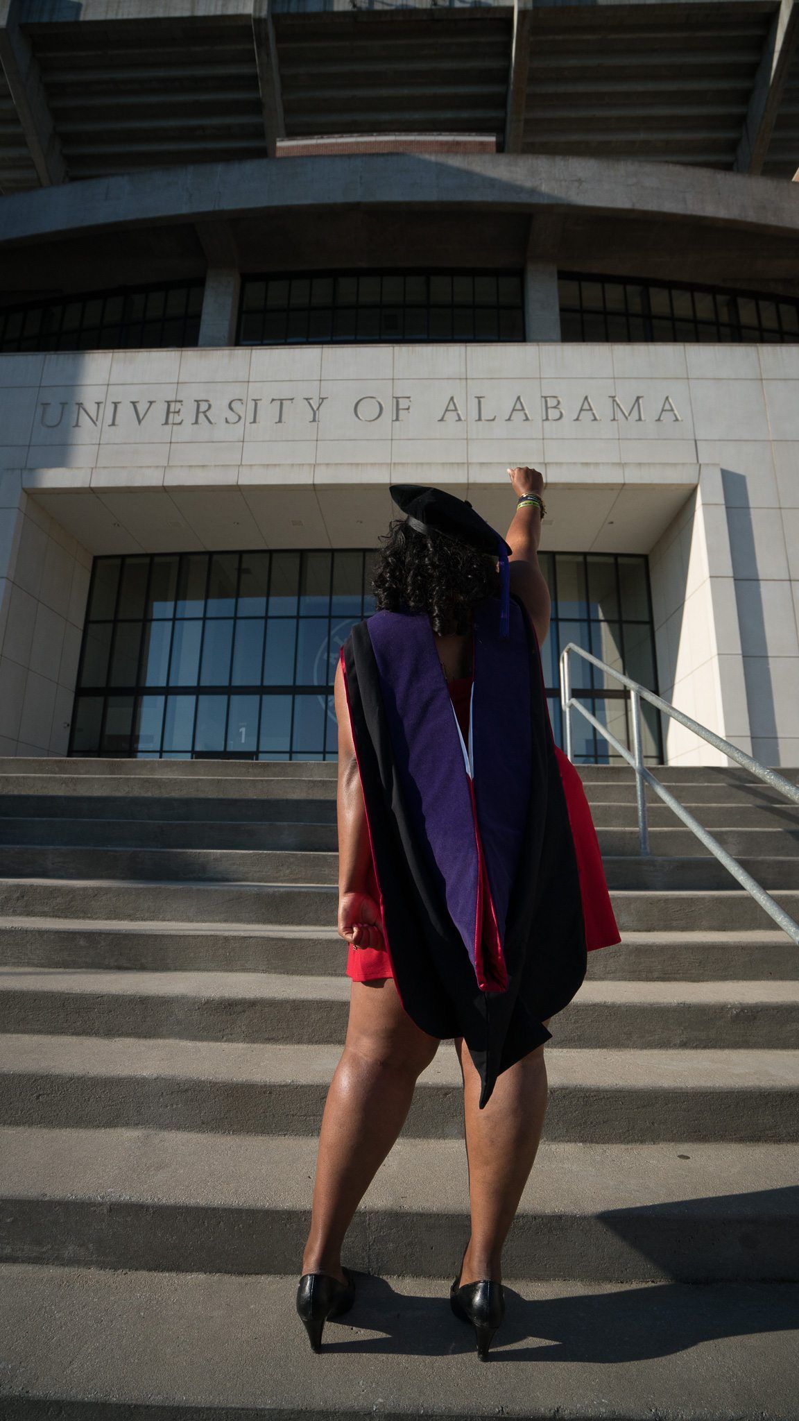 Graduate in purple gown posing on steps outside the University of Alabama.