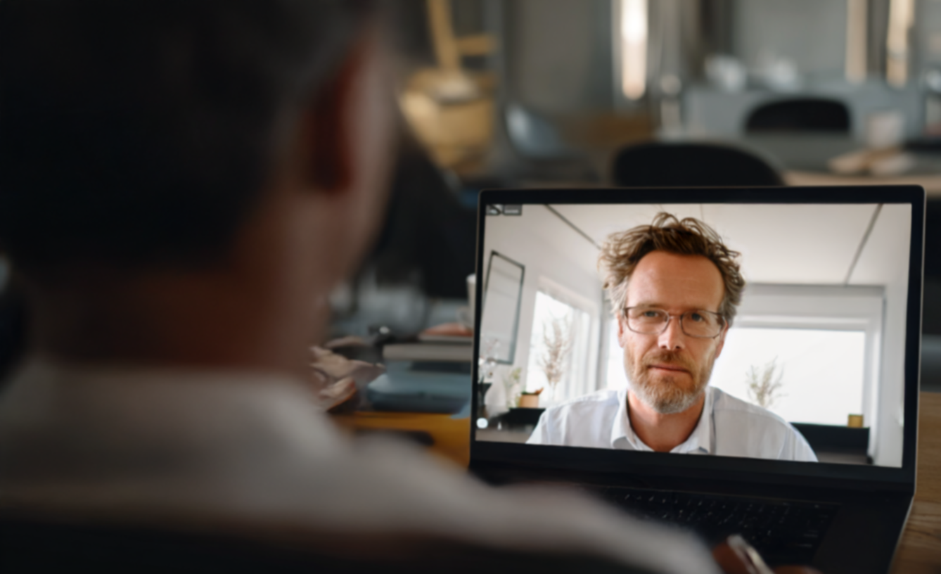 Person on video call with a man on a laptop screen; both men are indoors.