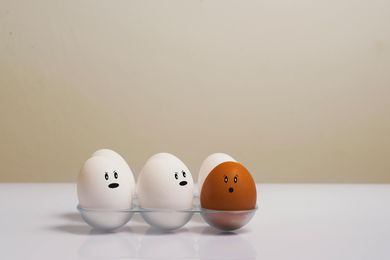 Three white eggs and a brown egg with drawn-on faces in an egg carton. The brown egg has a surprised expression.