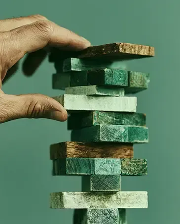Hand stacking wooden blocks in a teal-green Jenga tower, with pieces jutting out unevenly
