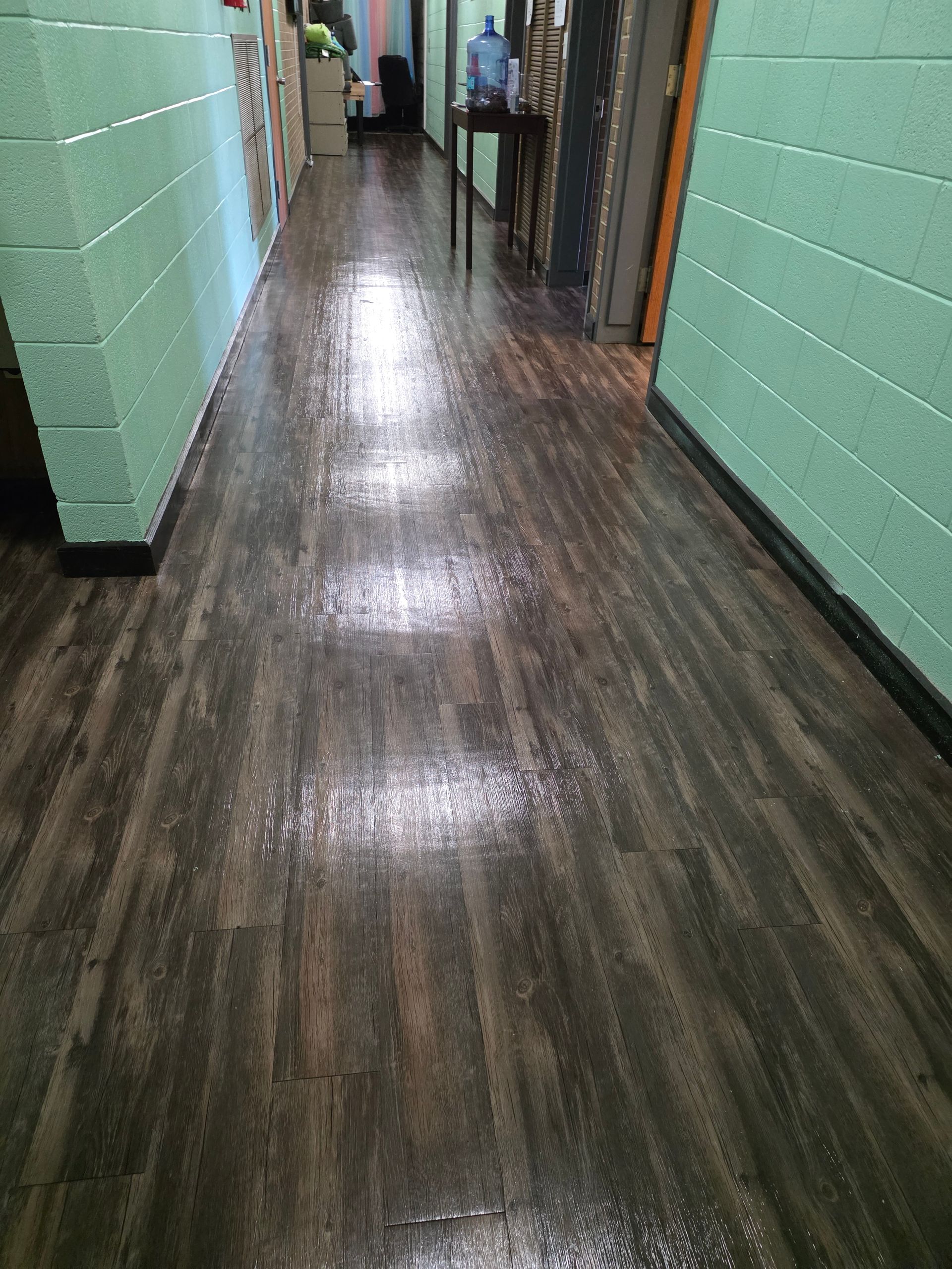 Dim hallway with mint green brick walls and a glossy dark wood floor, leading to a distant doorway.
