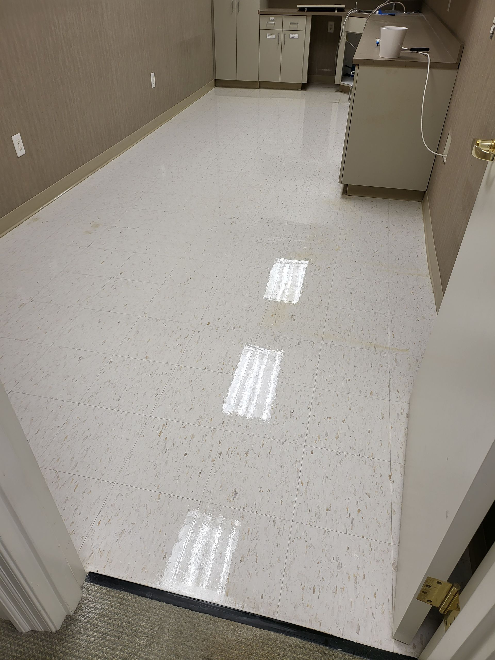 A room with a white floor and a kitchen in the background