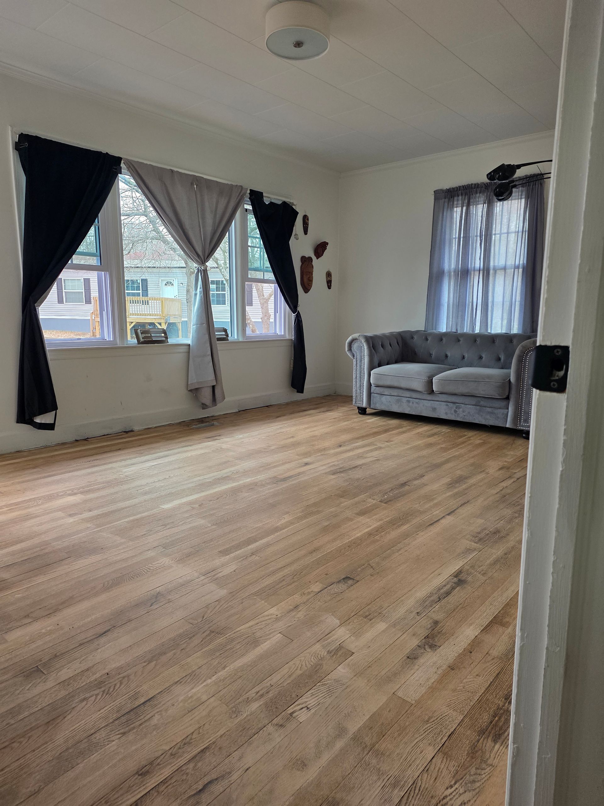 A living room with hardwood floors and a fan in the background.