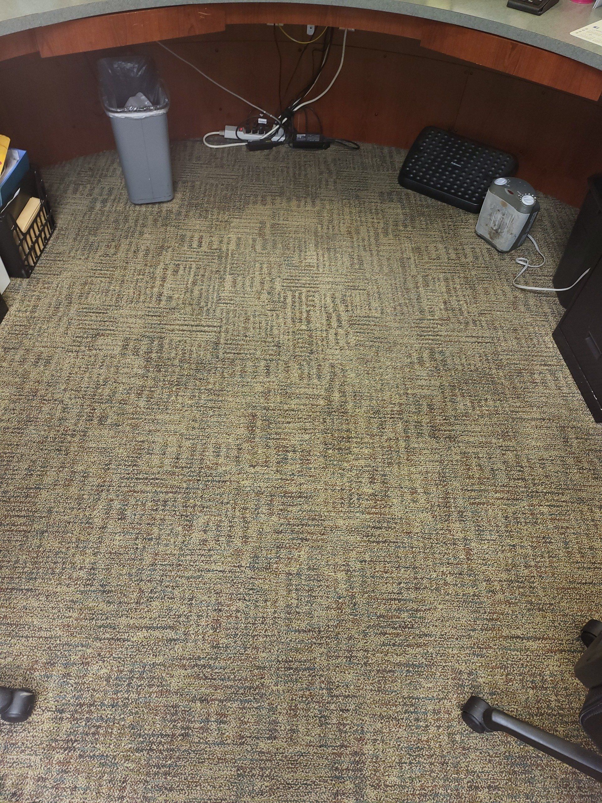 A carpeted floor in an office with a desk and chair.