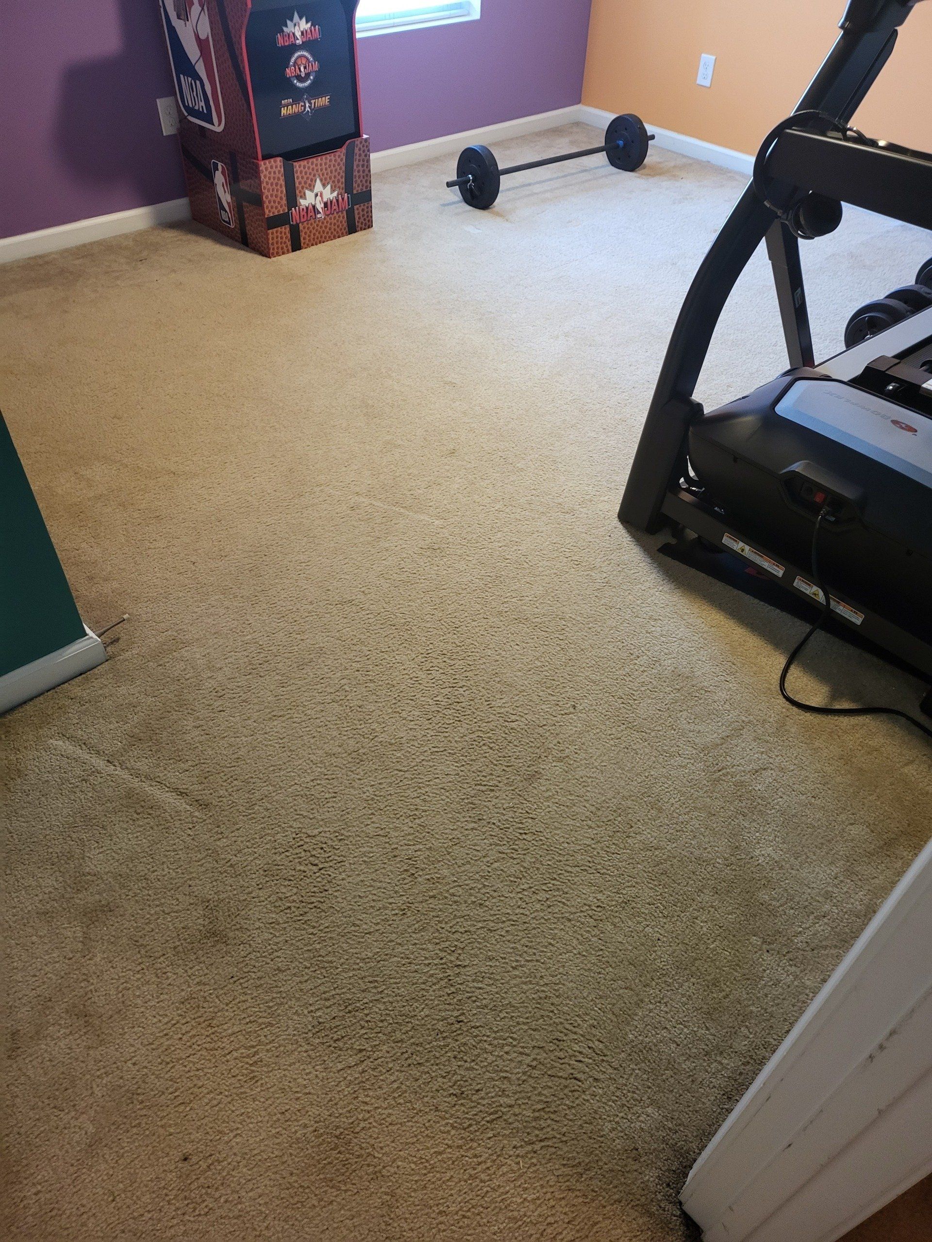 A gym with a treadmill and a barbell on the floor