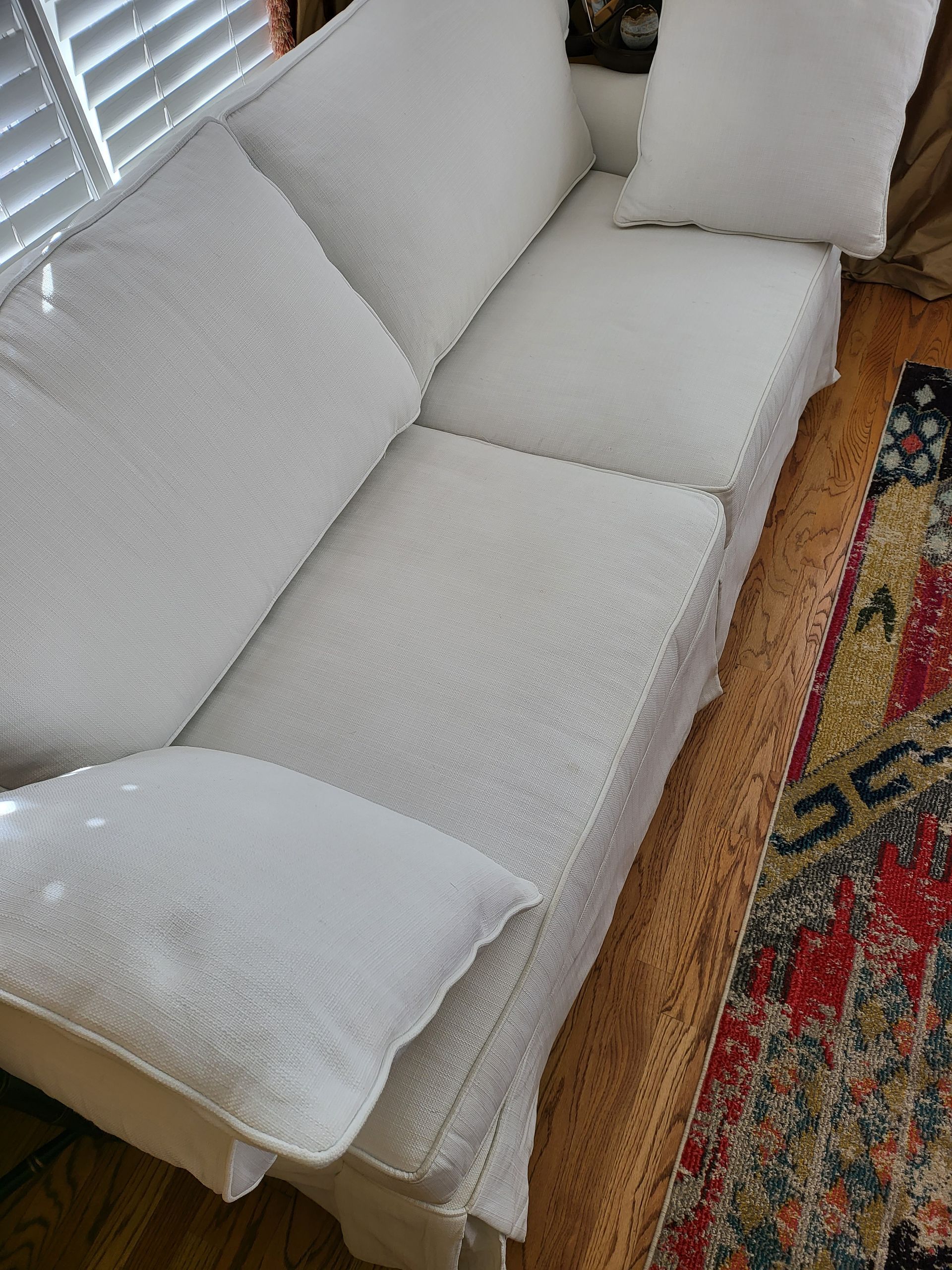 A white couch is sitting on a wooden floor next to a rug.