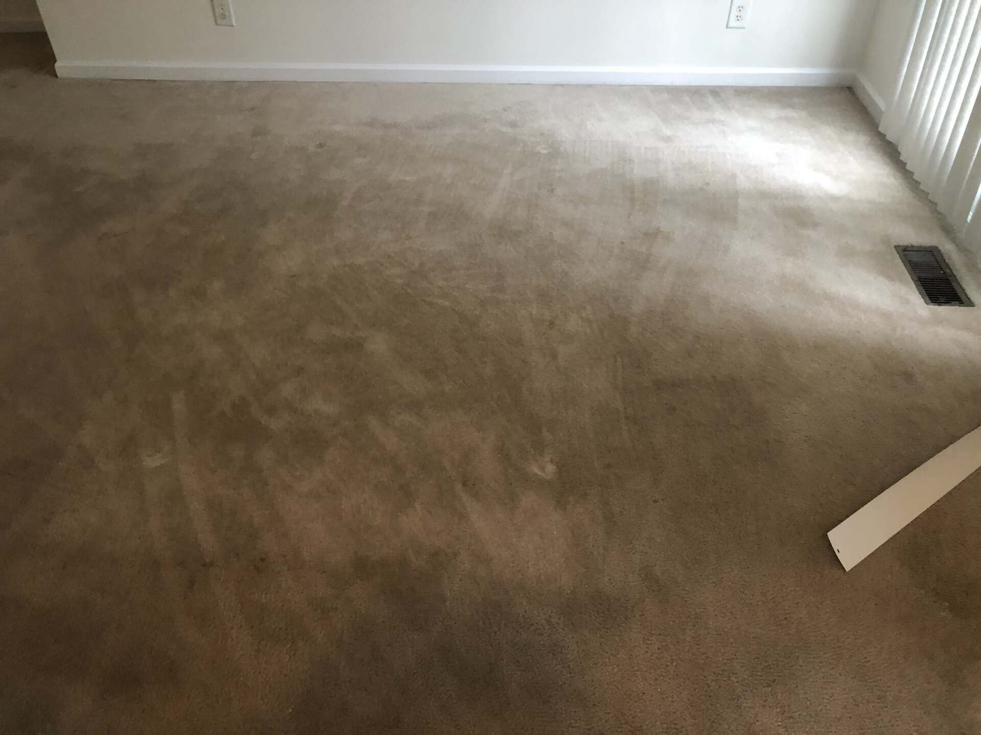 A living room with a carpeted floor and a window.