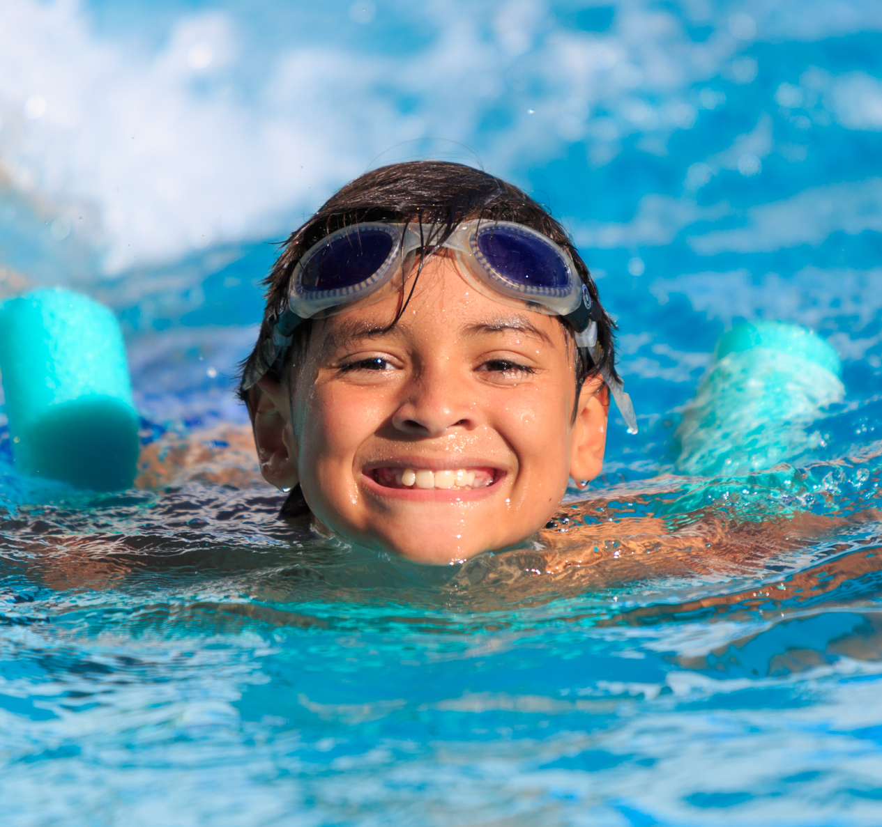 A young boy wearing goggles is swimming in a pool.