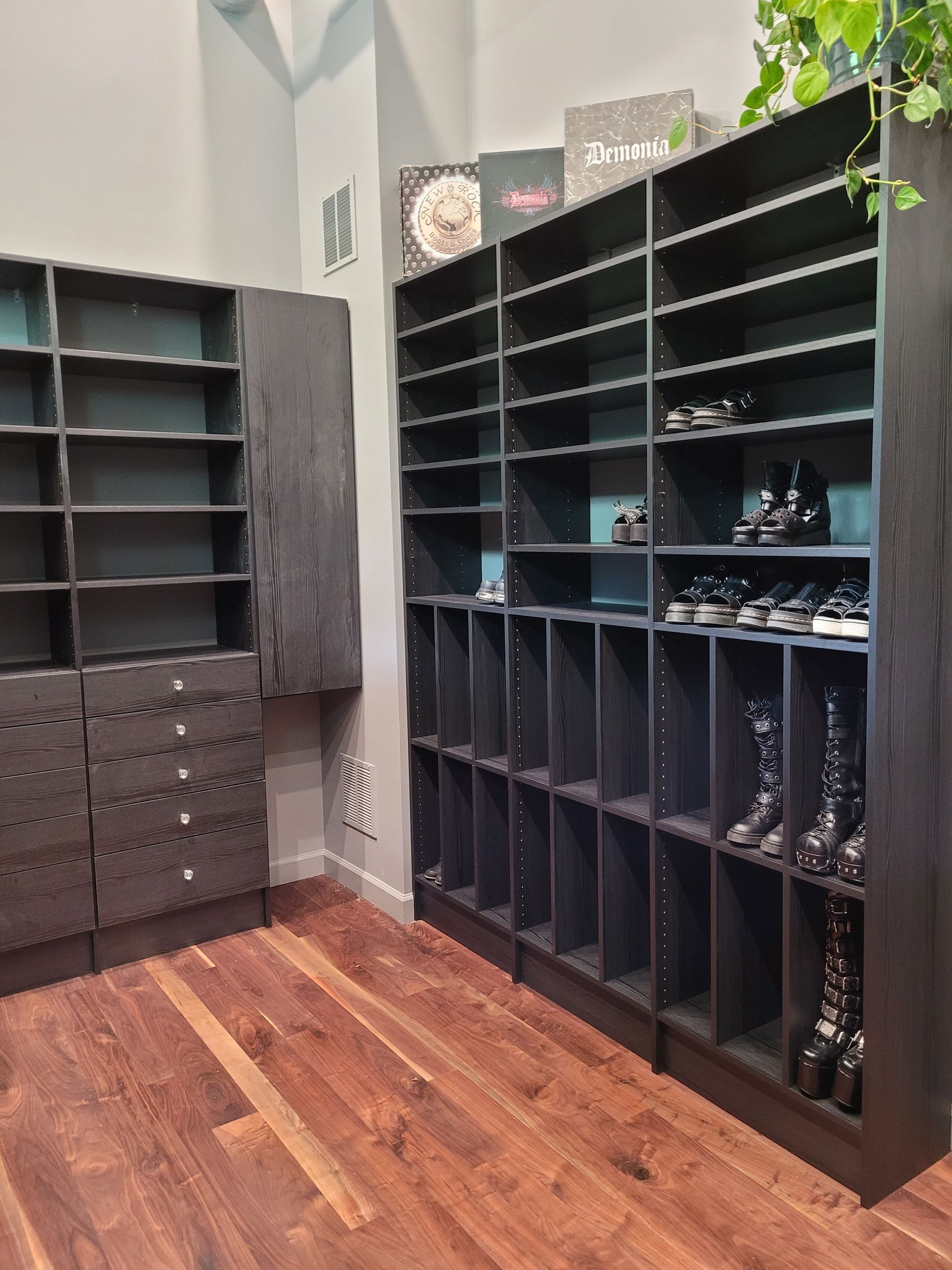A small shoe storage room with black cubby shelves, drawers, and a wood floor.