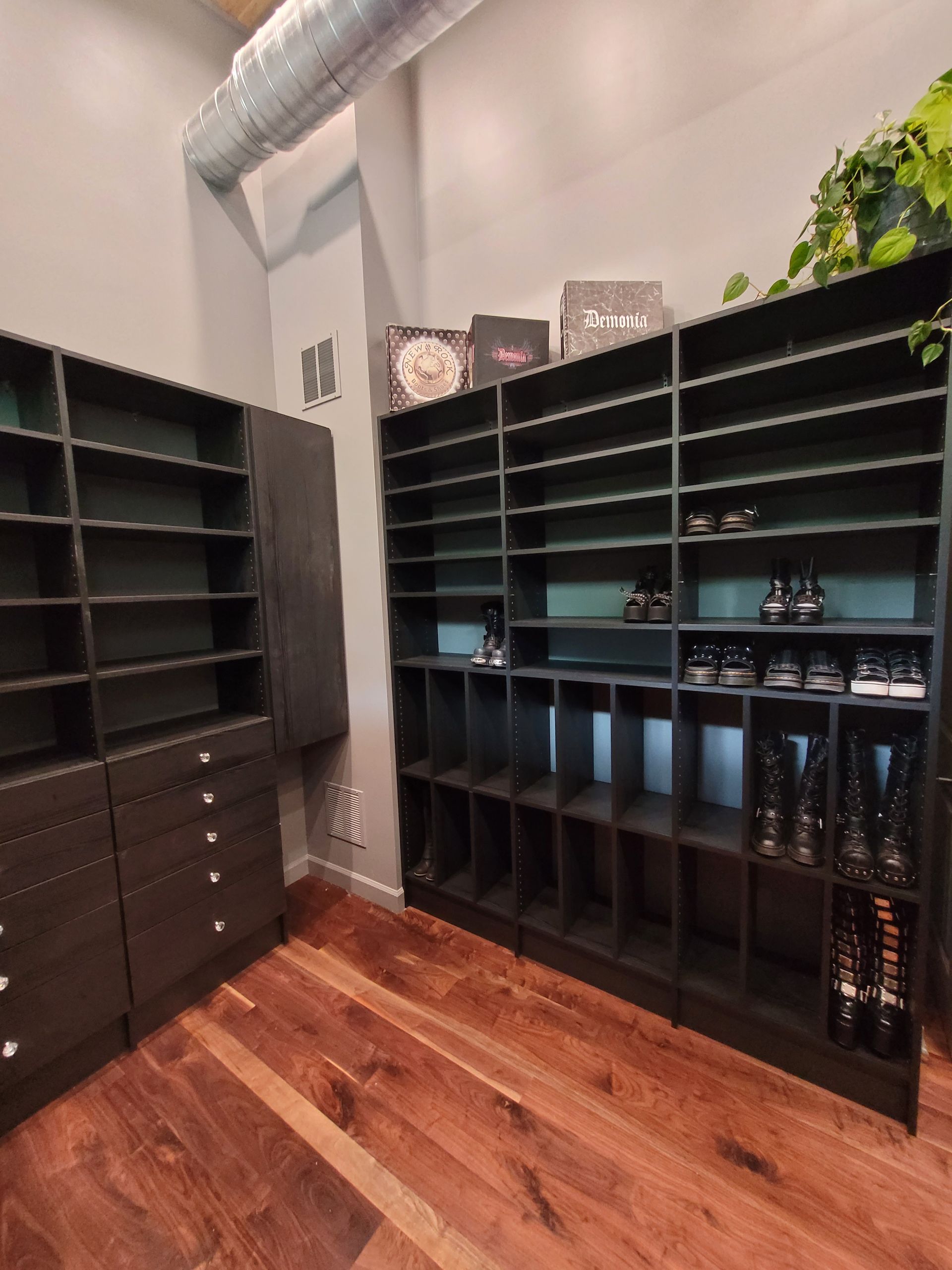 Walk-in closet with black shelving units, hanging rods, and hardwood floor.
