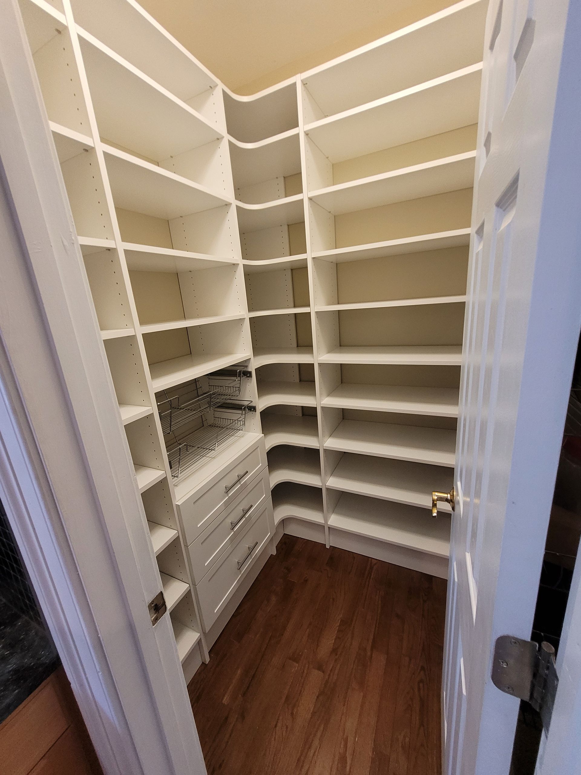 Empty walk-in closet with white shelves and a wood floor, viewed through an open door.
