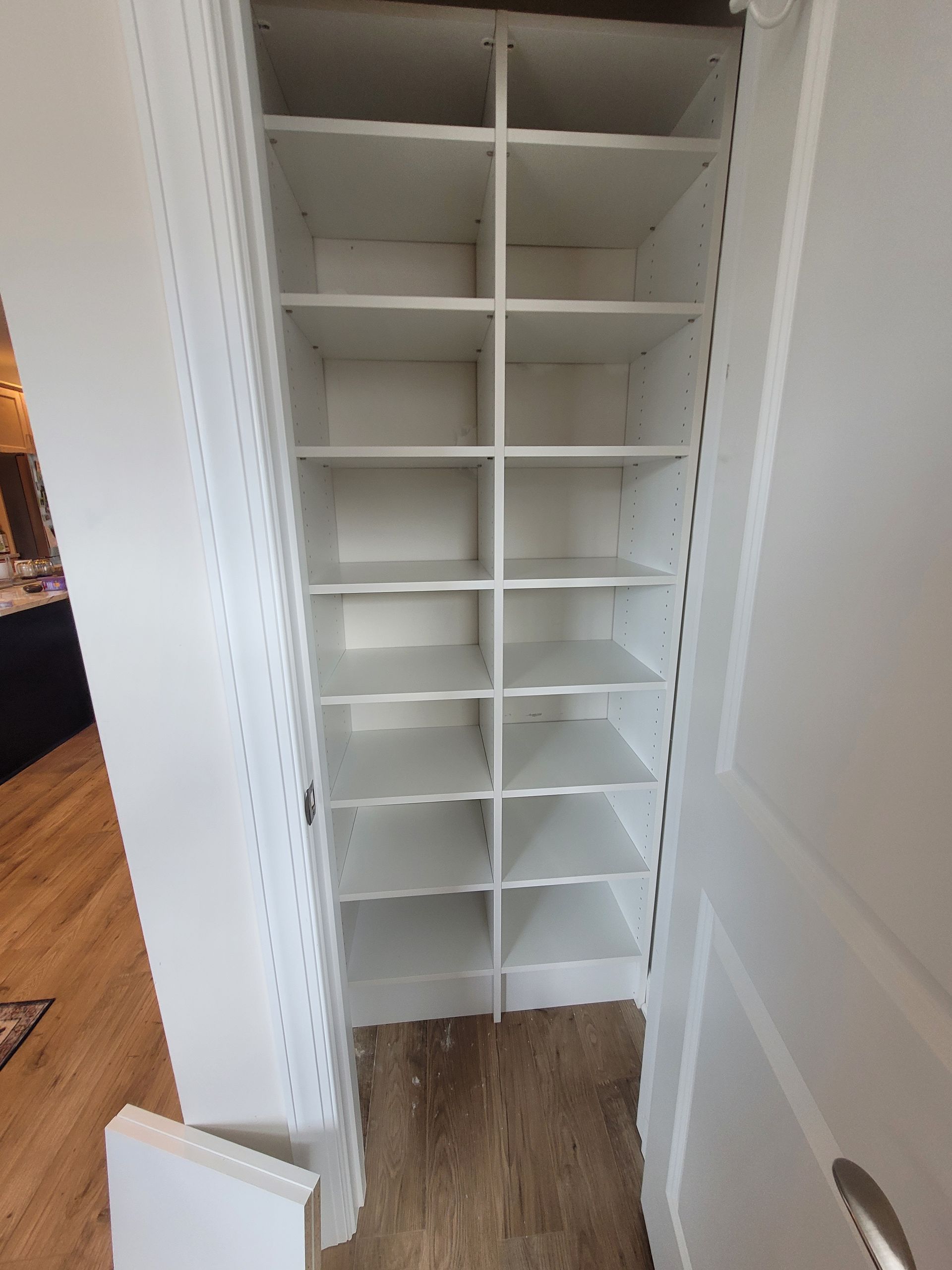 Empty white closet with built-in shelves and wood floor, viewed through open doors