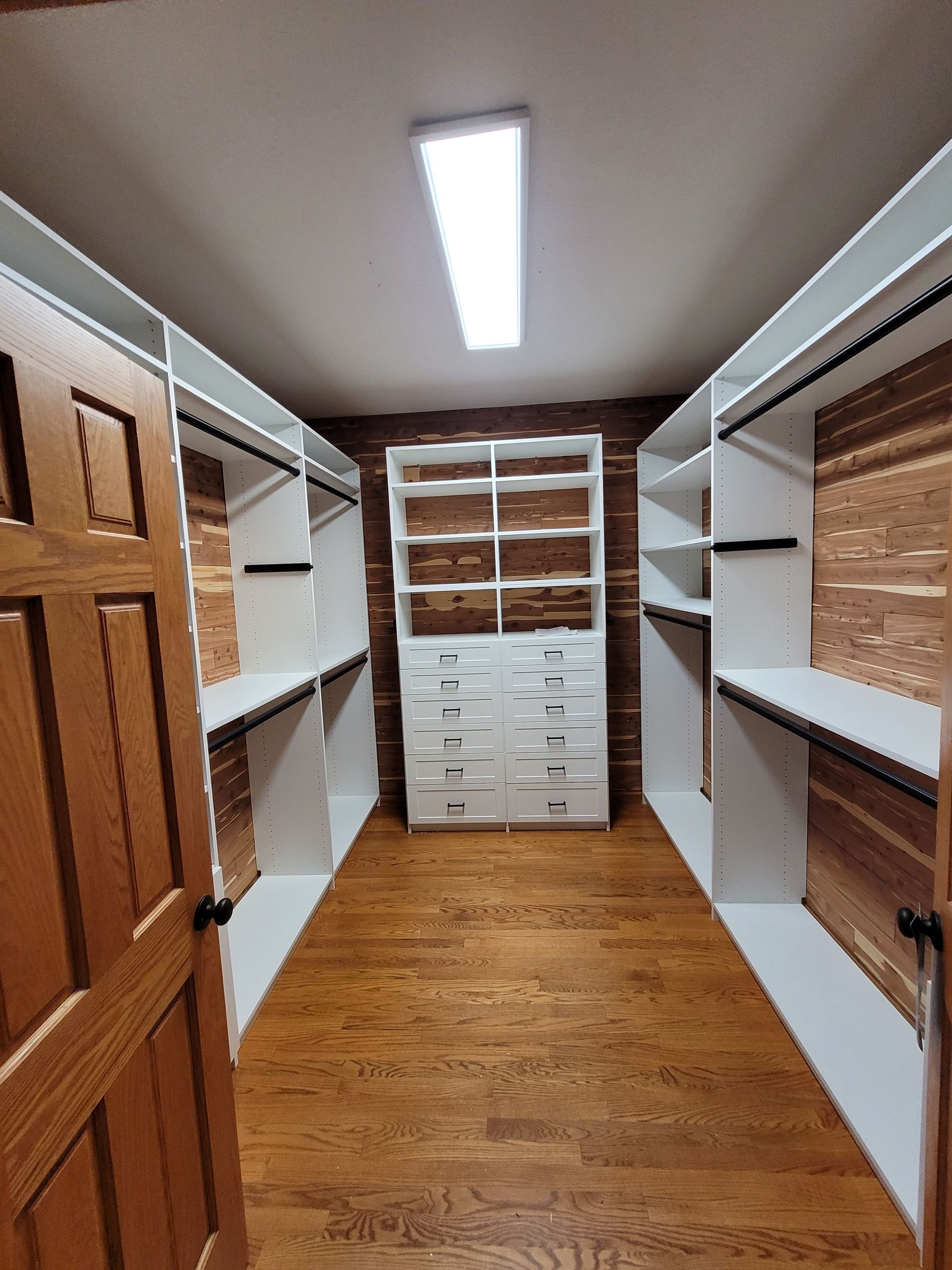 Walk-in closet with white shelving, drawers, and hanging rods, viewed from the doorway.