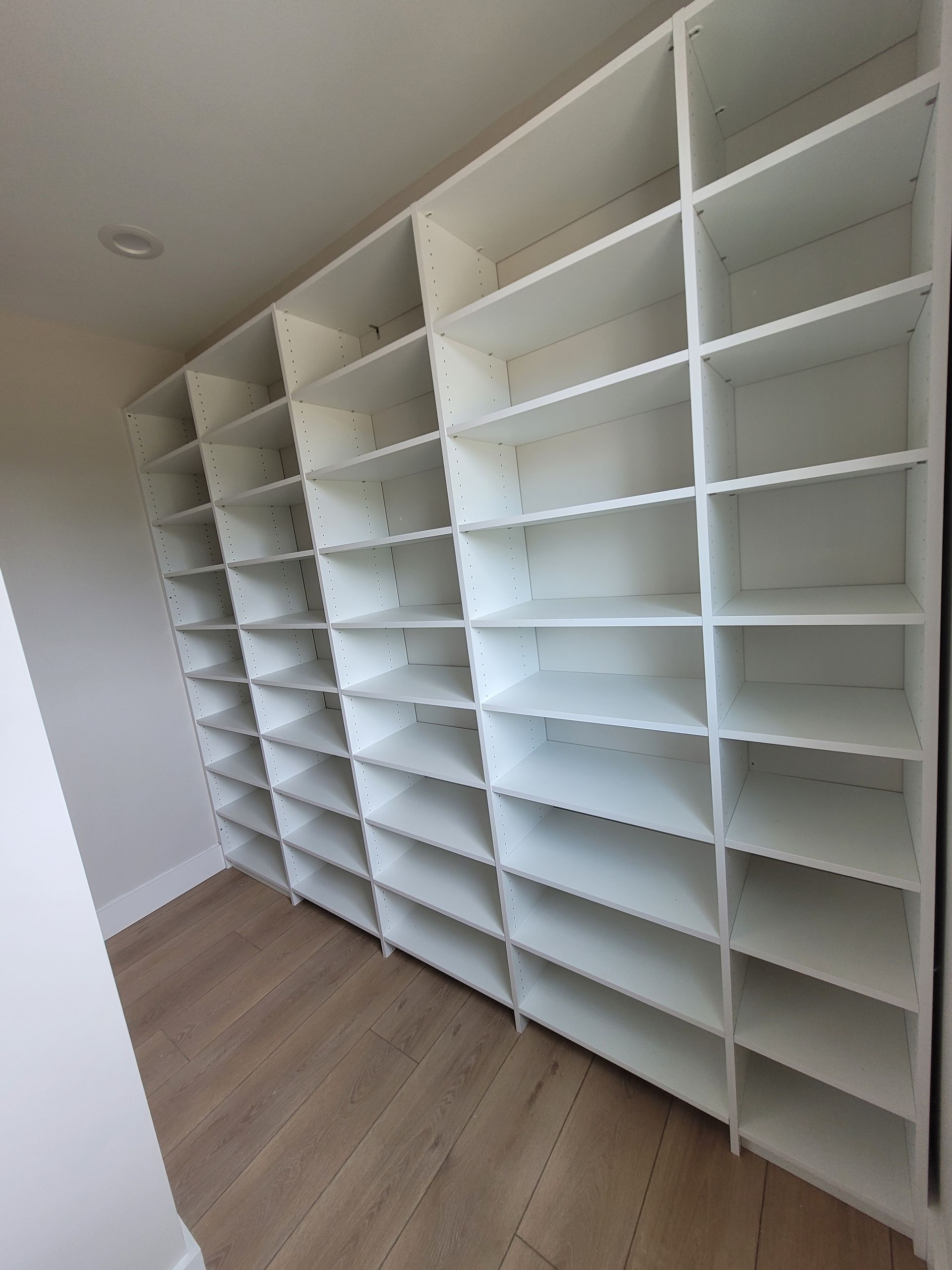 White wall-mounted shelving units in an empty room with light wood flooring.