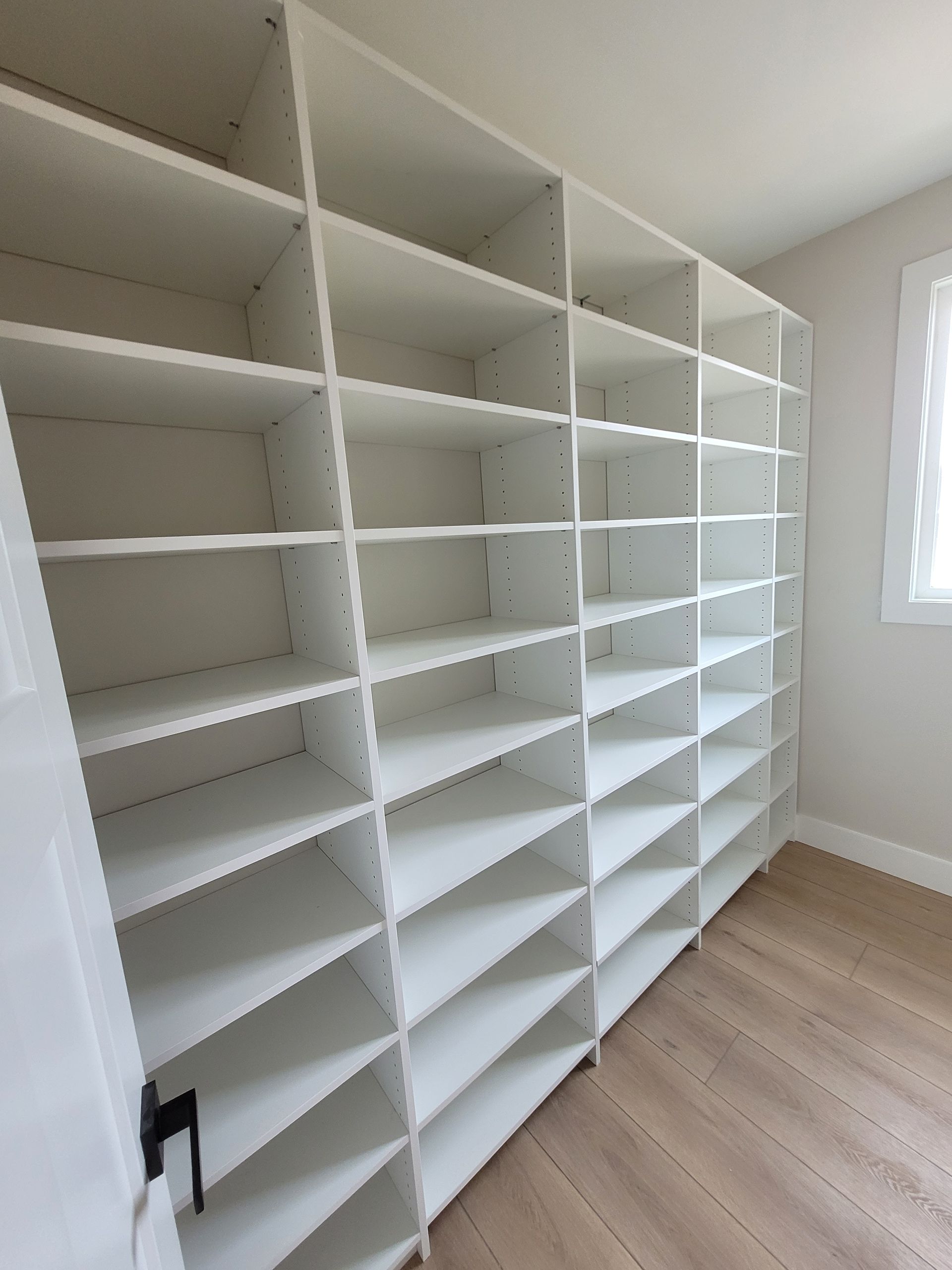 White built-in shelving units in a bright empty room with a window and light wood floor.