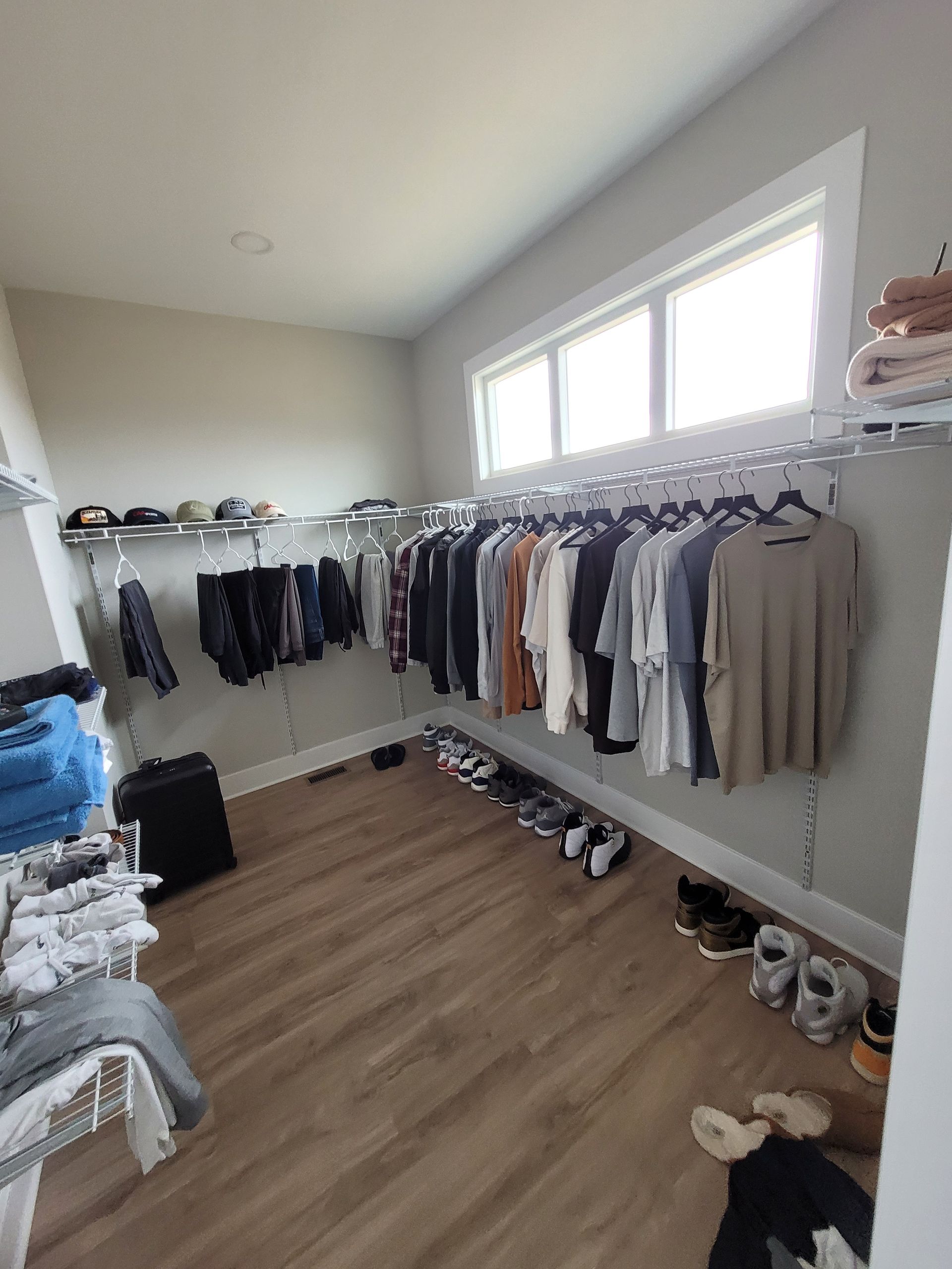Walk-in closet with clothes hanging on both sides, shoes on the floor, and shelves with folded items.