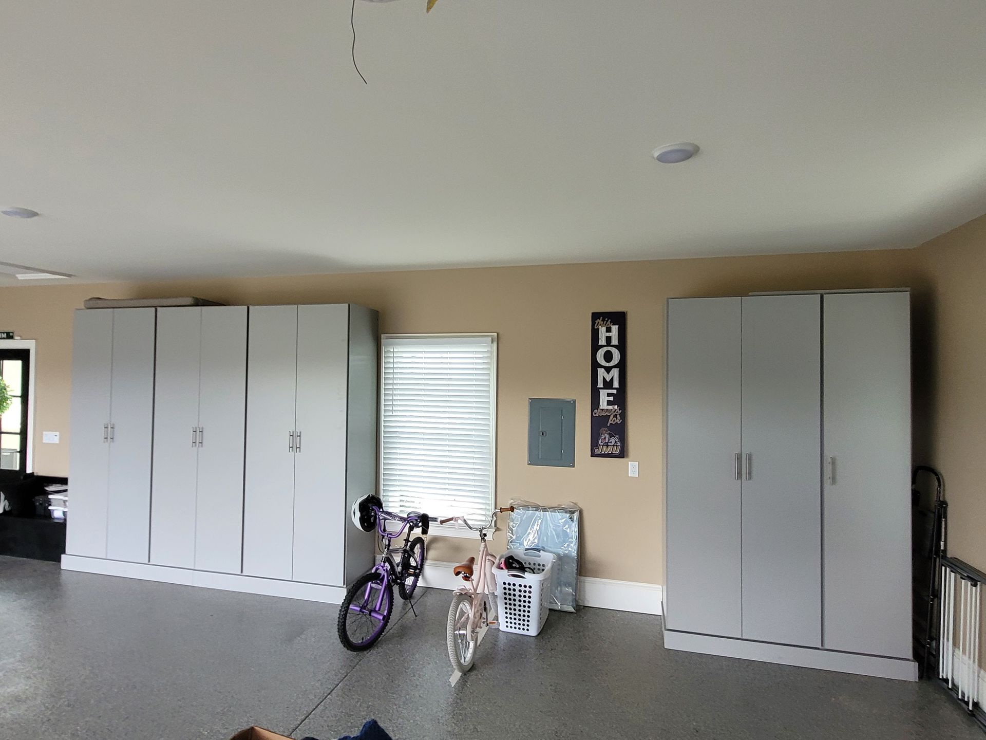 Garage interior with gray storage cabinets, a bicycle, a child’s tricycle, and a HOME sign on the wall