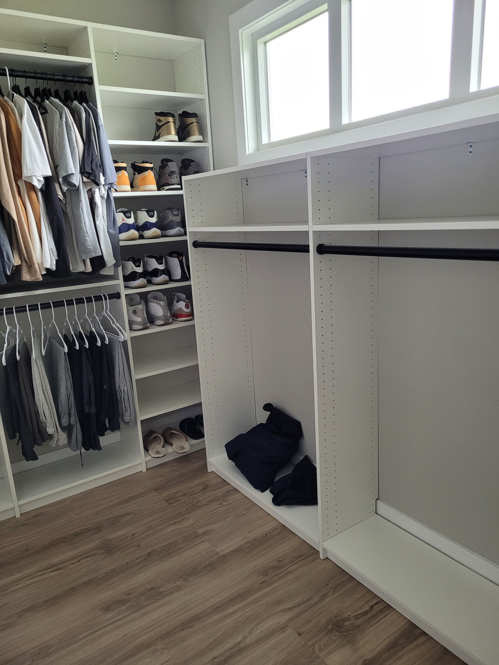 Walk-in closet with hanging clothes, shelves of shoes, and white built-in storage by a window
