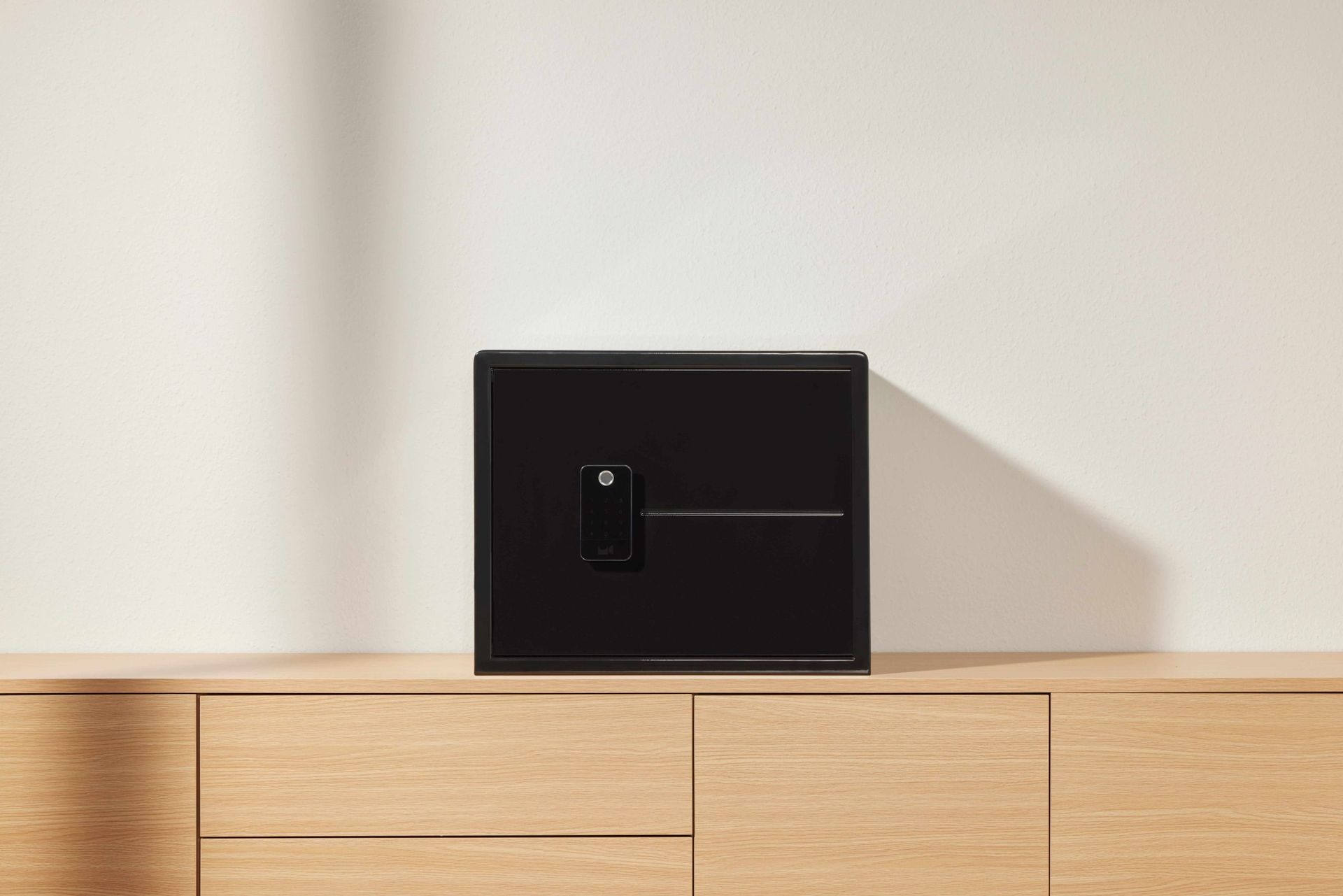 Black wall-mounted control panel on a light wood cabinet against a plain white wall.