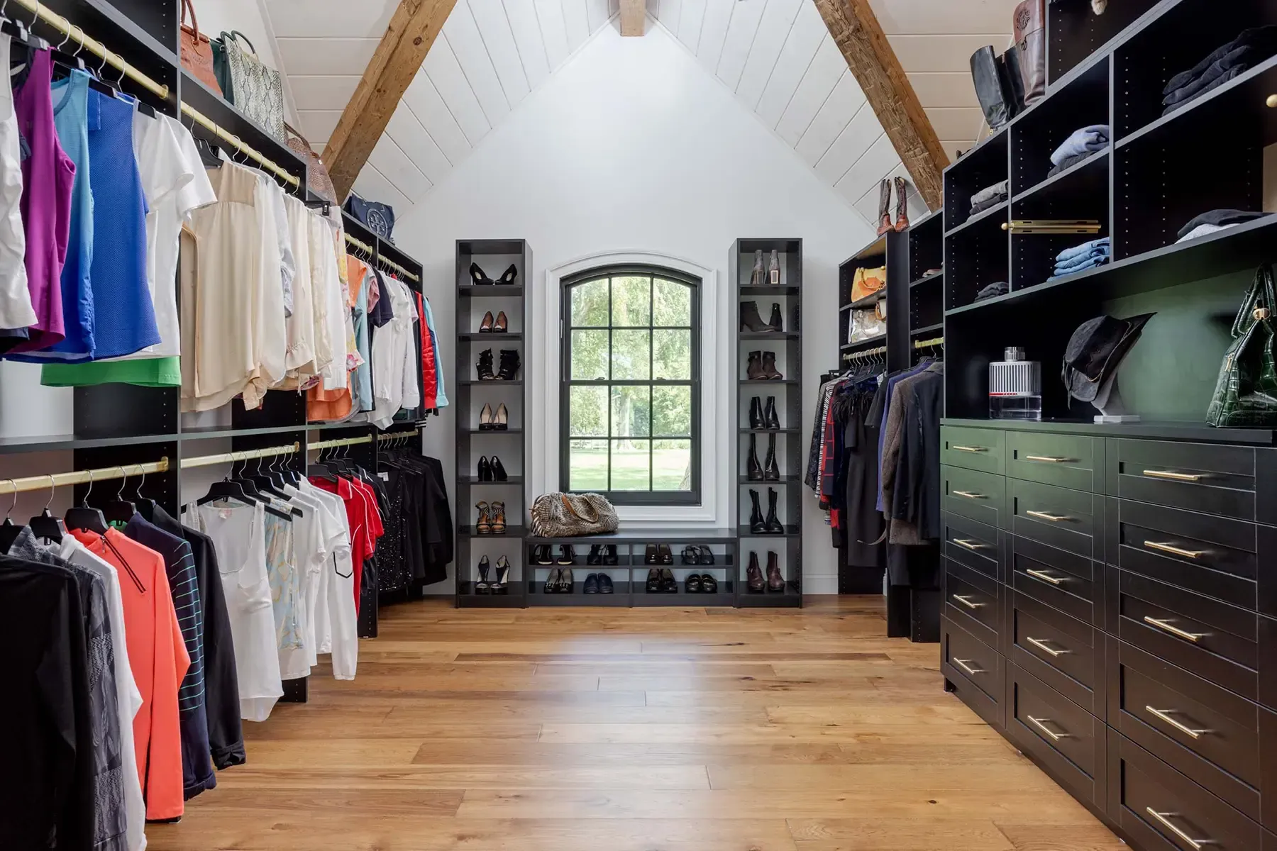Walk-in closet with hanging clothes, drawers, and a window at the far end