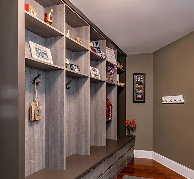 Built-in gray mudroom cubbies with hooks and shelves beside a bench in a tan hallway