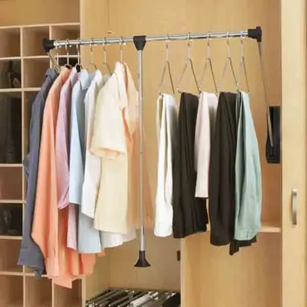 Clothes hanging on a rack inside a wooden wardrobe, with shirts and pants in neutral and pastel colors