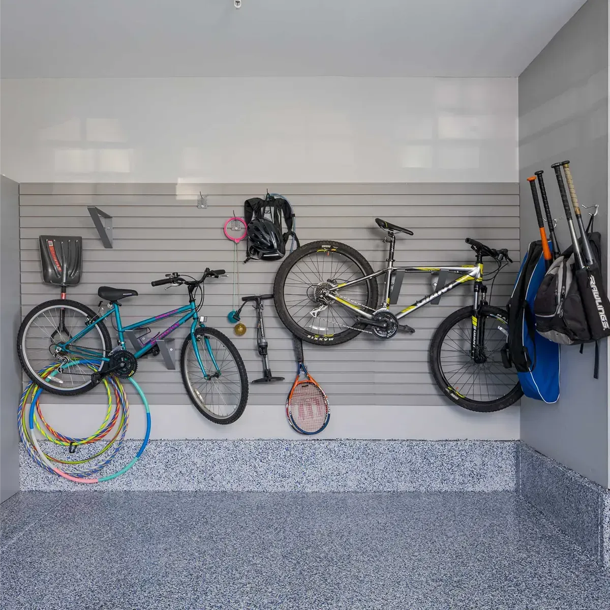 Garage wall with two bicycles, hanging gear, and colorful bike rims on slatwall storage.