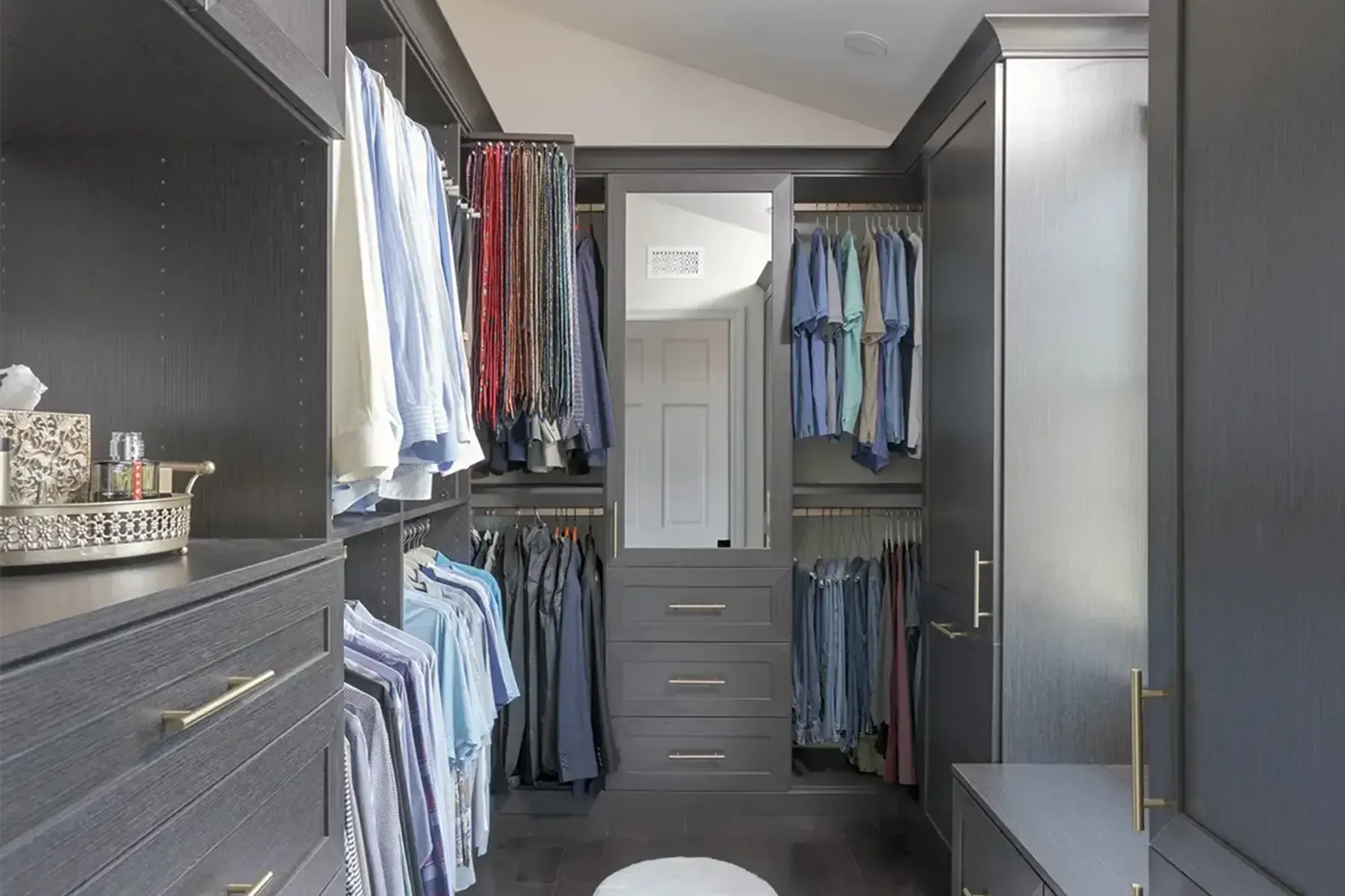 Modern walk-in closet with hanging clothes, drawers, and shelves in gray cabinetry
