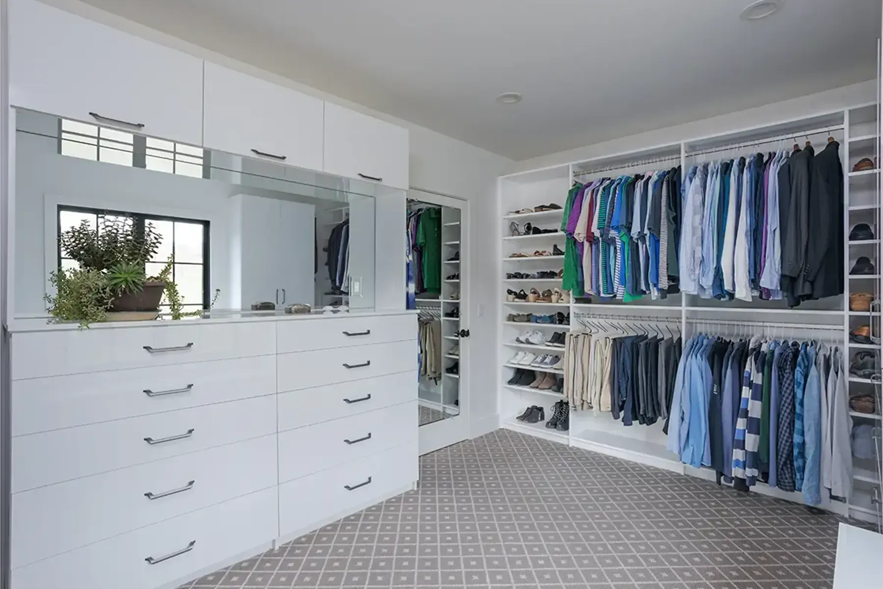 Bright white walk-in closet with drawers, mirrored cabinets, and neatly organized clothes on shelves and hanging rods