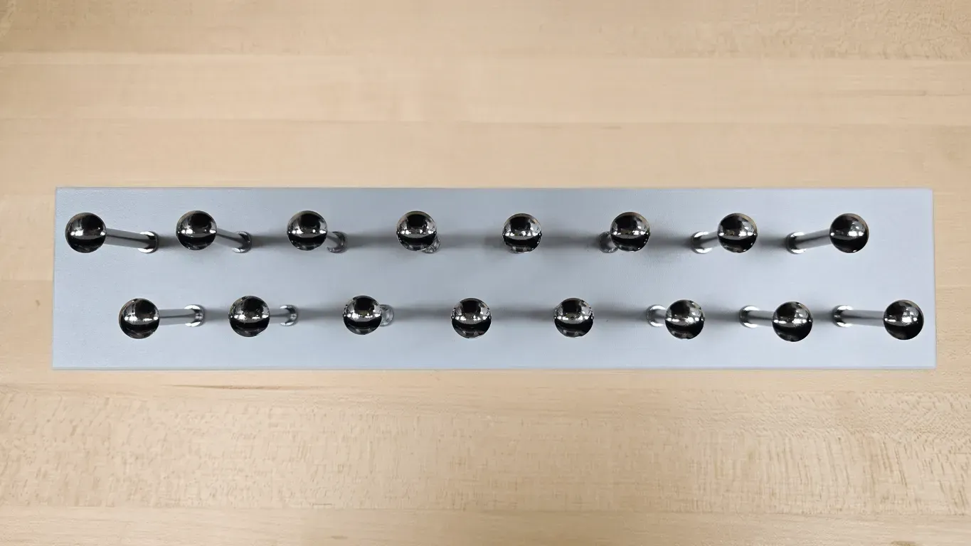 Two rows of shiny metal balls connected by rods on a light wood surface.