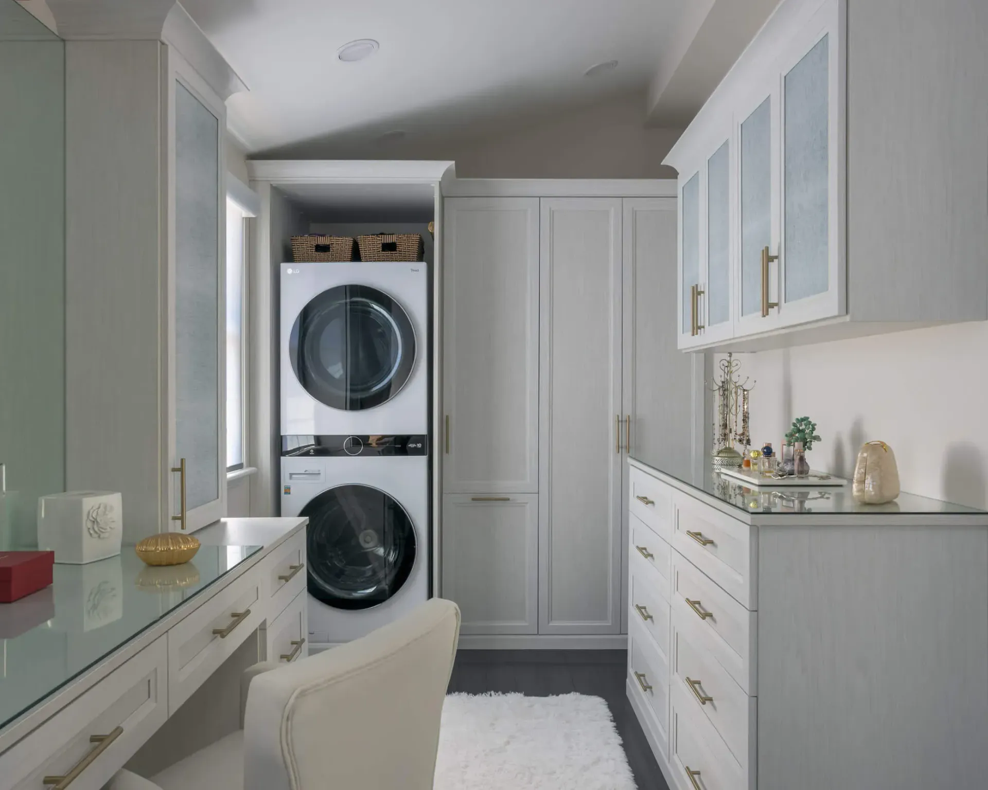 Bright laundry room with stacked washer and dryer, white cabinets, and a vanity-style counter.