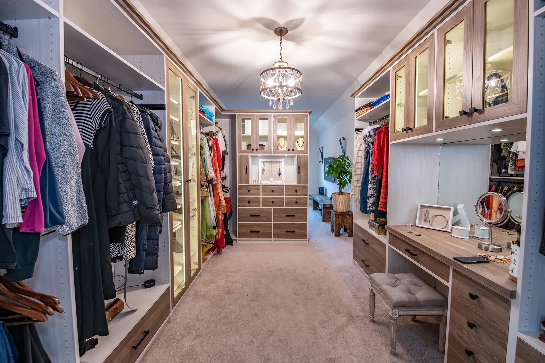 Spacious walk-in closet with built-in shelving, hanging clothes, drawers, and a carpeted central aisle.