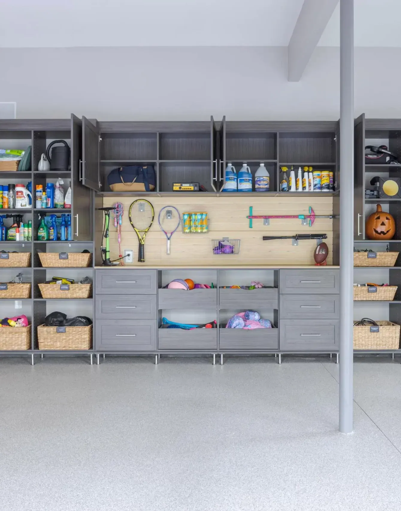 Grey garage storage wall with shelves, baskets, sports gear, and cabinets neatly organized