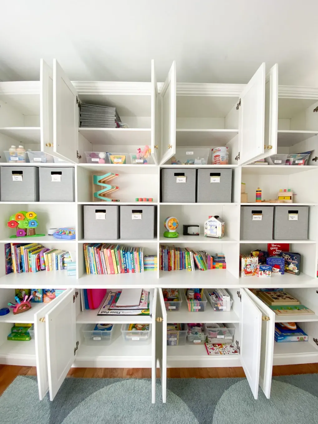 White children’s storage shelves with open bins, books, and toys in a bright playroom
