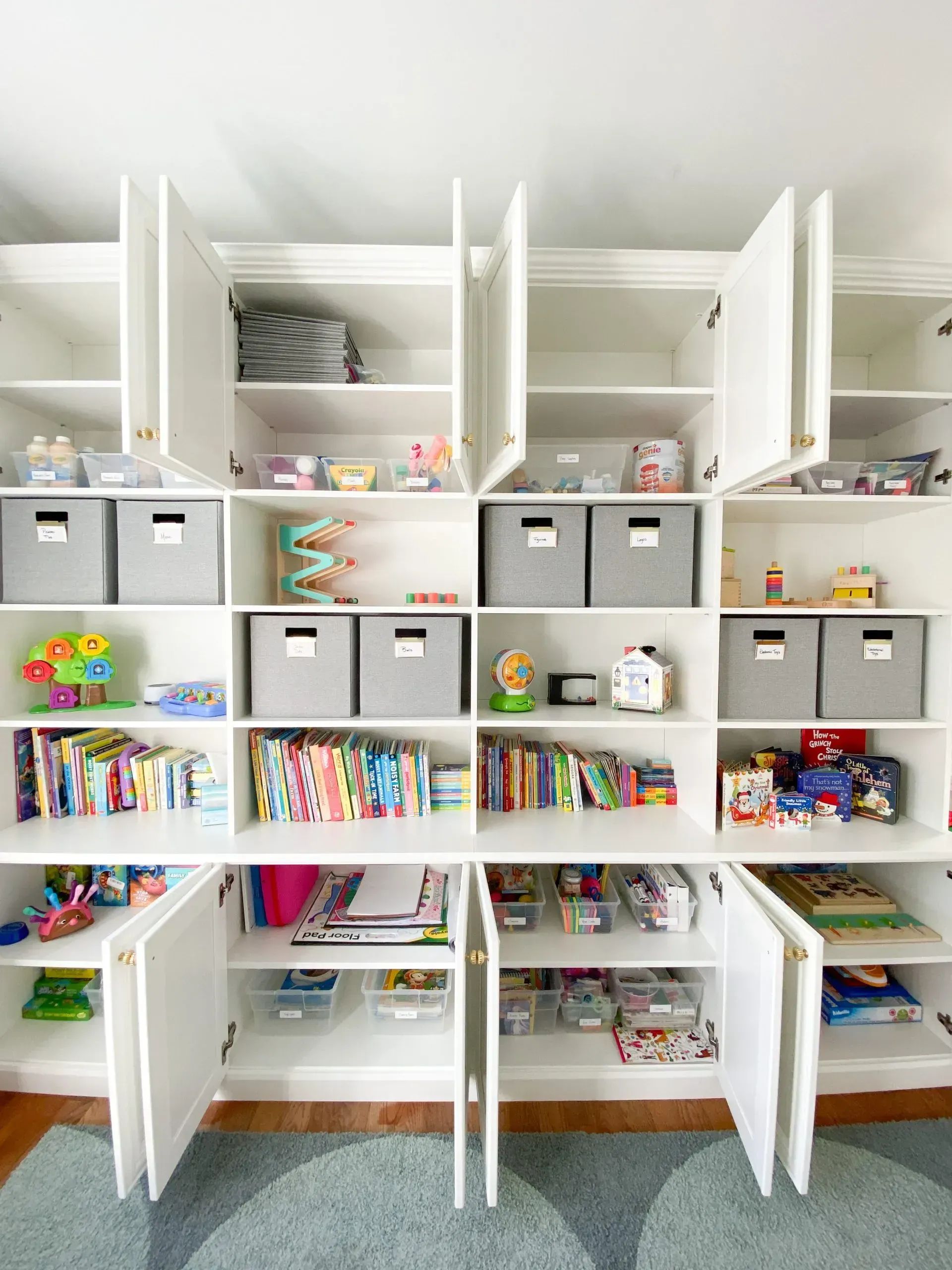 White children’s storage shelves with open bins, books, and toys in a bright playroom