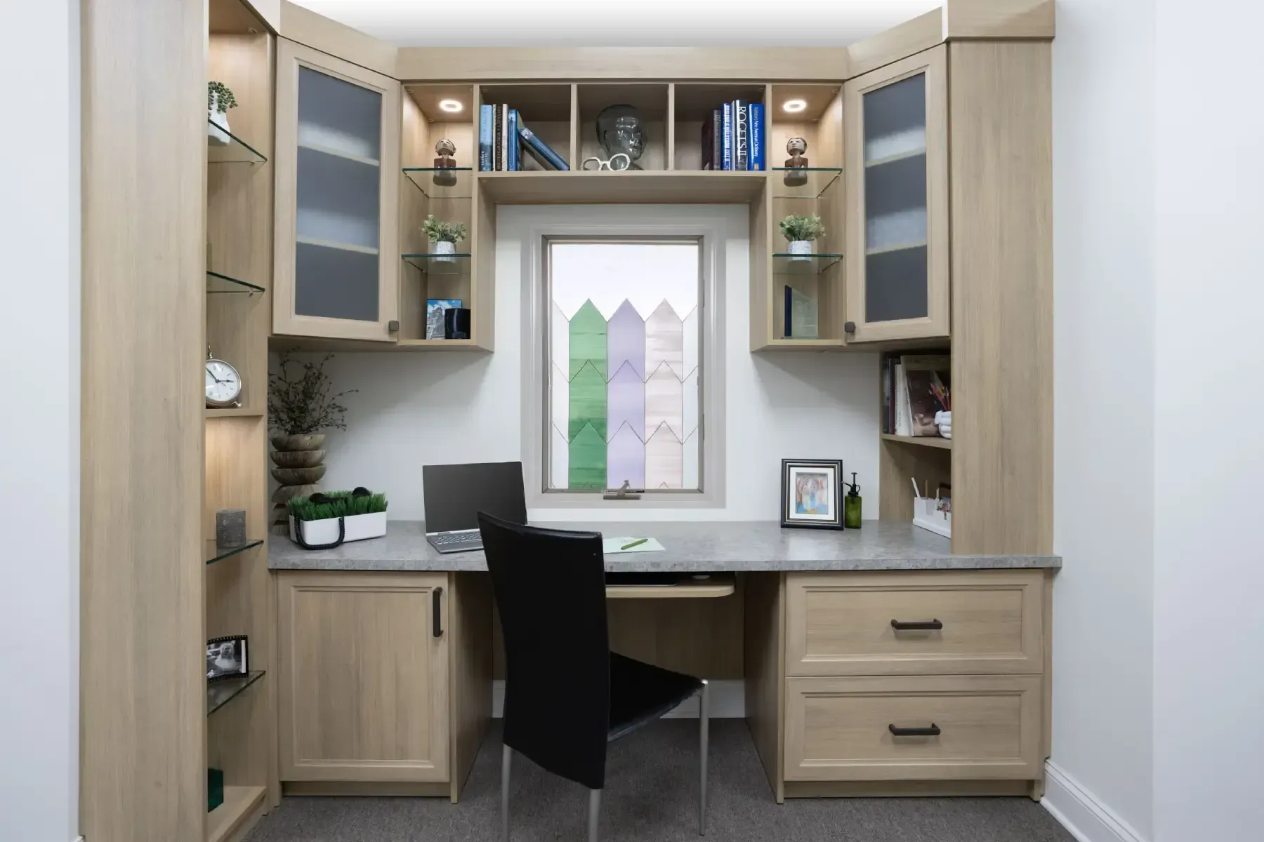 Built-in home office with desk, black chair, cabinets, and computer by a window