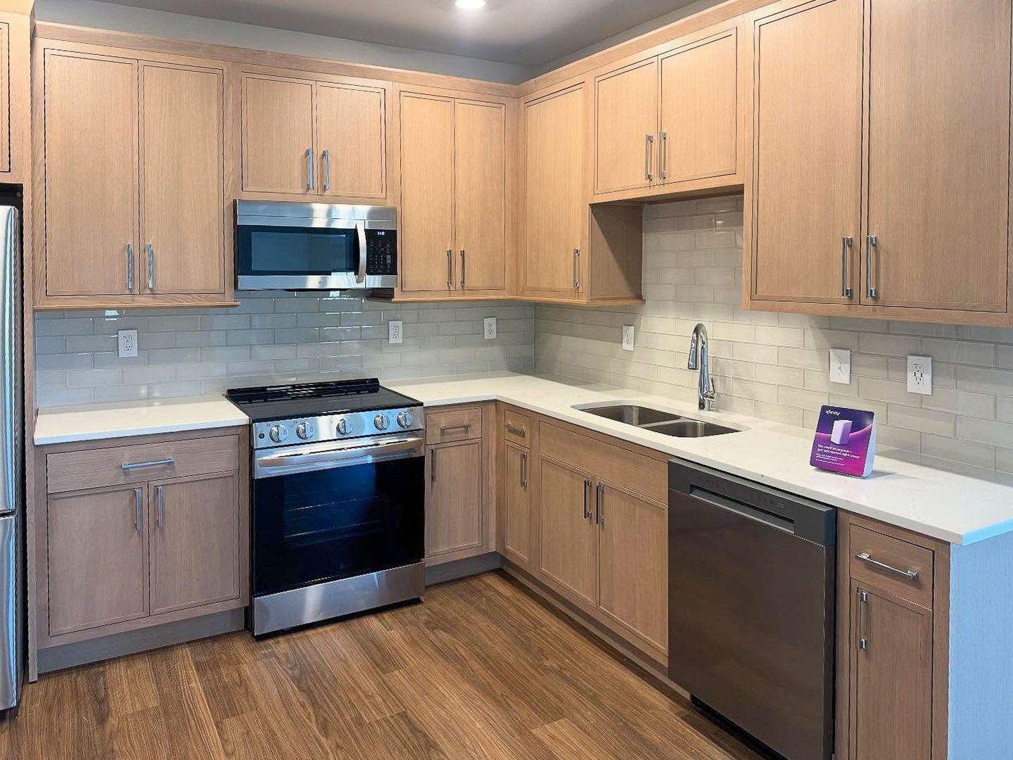 A modern kitchen with light wood cabinets, stainless steel appliances, white countertops, and a light-colored backsplash.