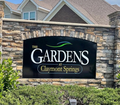 Stone entrance sign reading “The Gardens at Claymont Springs” in front of houses and shrubs