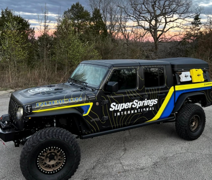 Black off-road truck with Super Springs branding parked outdoors at dusk, blue and yellow accents.