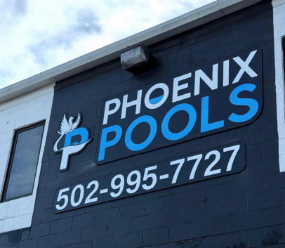 Phoenix Pools sign on a dark building with blue and white lettering and phone number 502-995-7727
